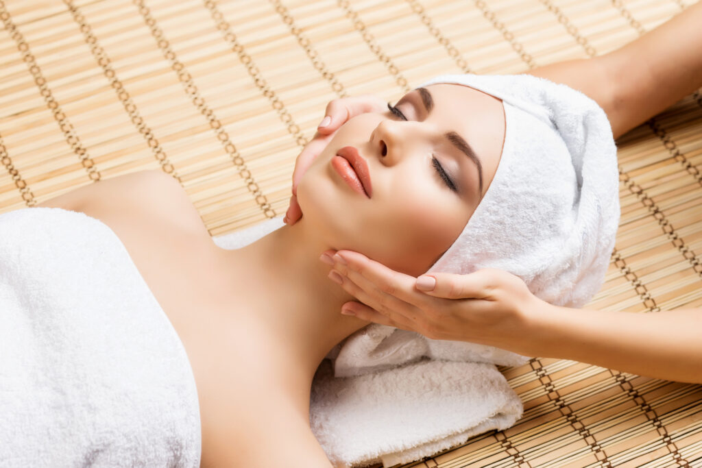 Beautiful, young and healthy woman on bamboo mat in spa salon having face massage. Spa, health and healing concept.